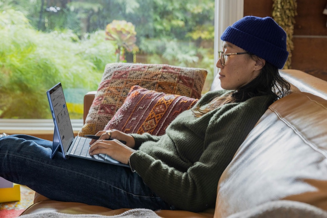 A woman sitting on a couch with a laptop, working comfortably from home.